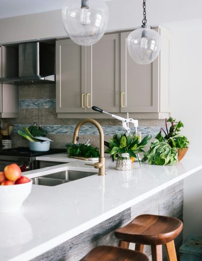 kitchen remodel Nicely designed white kitchen with lots of greenery, wooden bar stools and hanging lights.